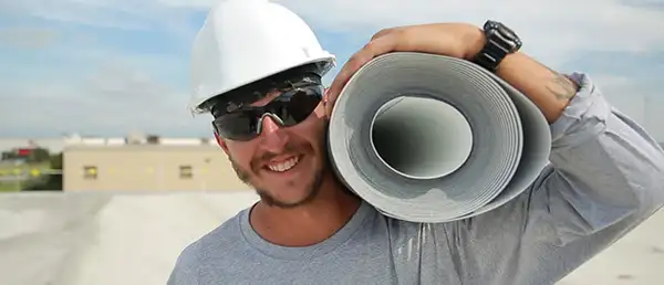 smiling roofer holding a roll of membrane